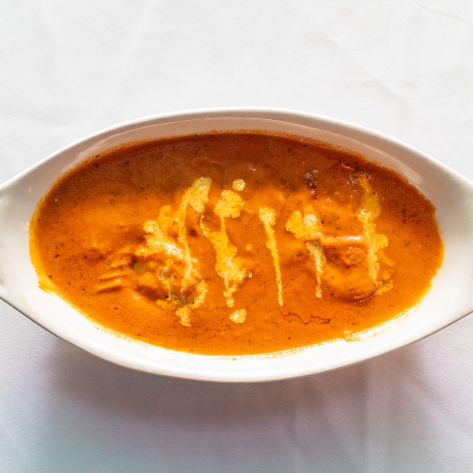 A white oval dish filled with orange curry, drizzled with white cream, on a white tablecloth.