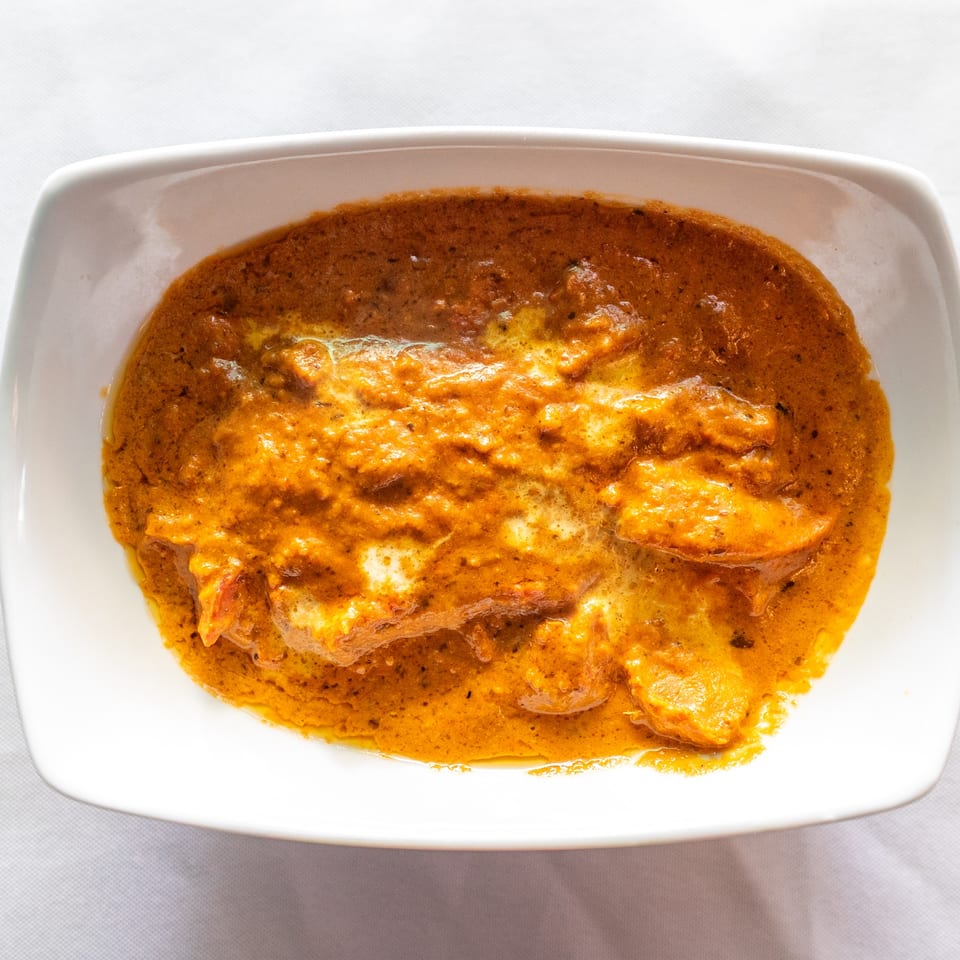 Close-up of a vibrant orange curry dish with white swirls, served in a white rectangular bowl.