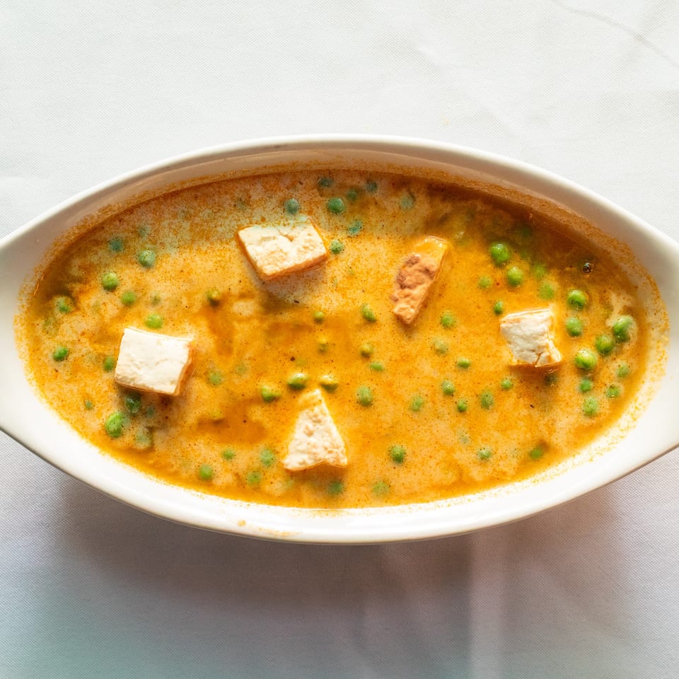Mutter Paneer, a creamy orange curry with green peas and paneer cheese cubes, in a white oval dish.
