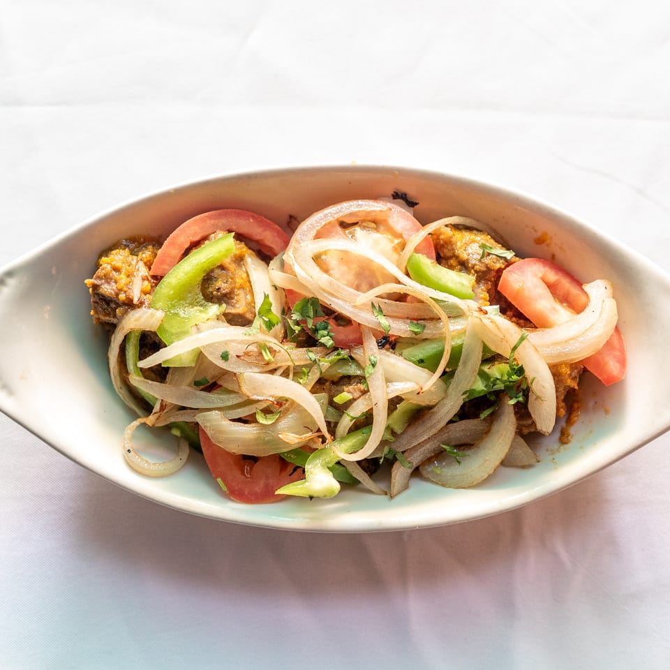 A white bowl filled with a dish of meat, sliced onions, green bell peppers, and tomatoes.