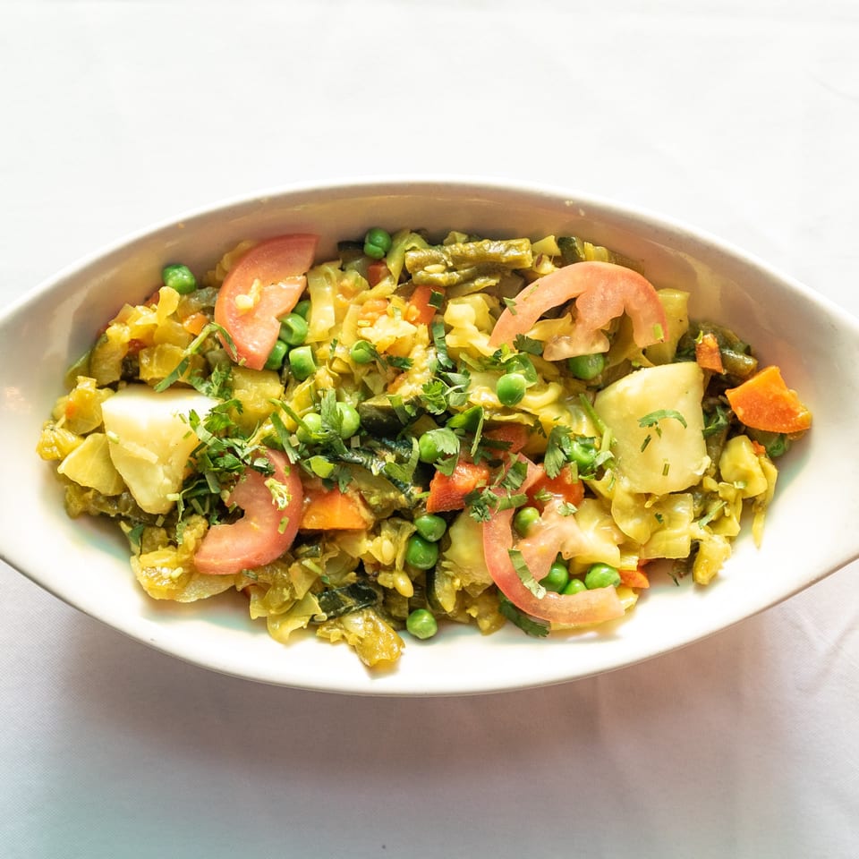 A white oval dish filled with mixed vegetables, including cabbage, peas, carrots, and tomatoes.