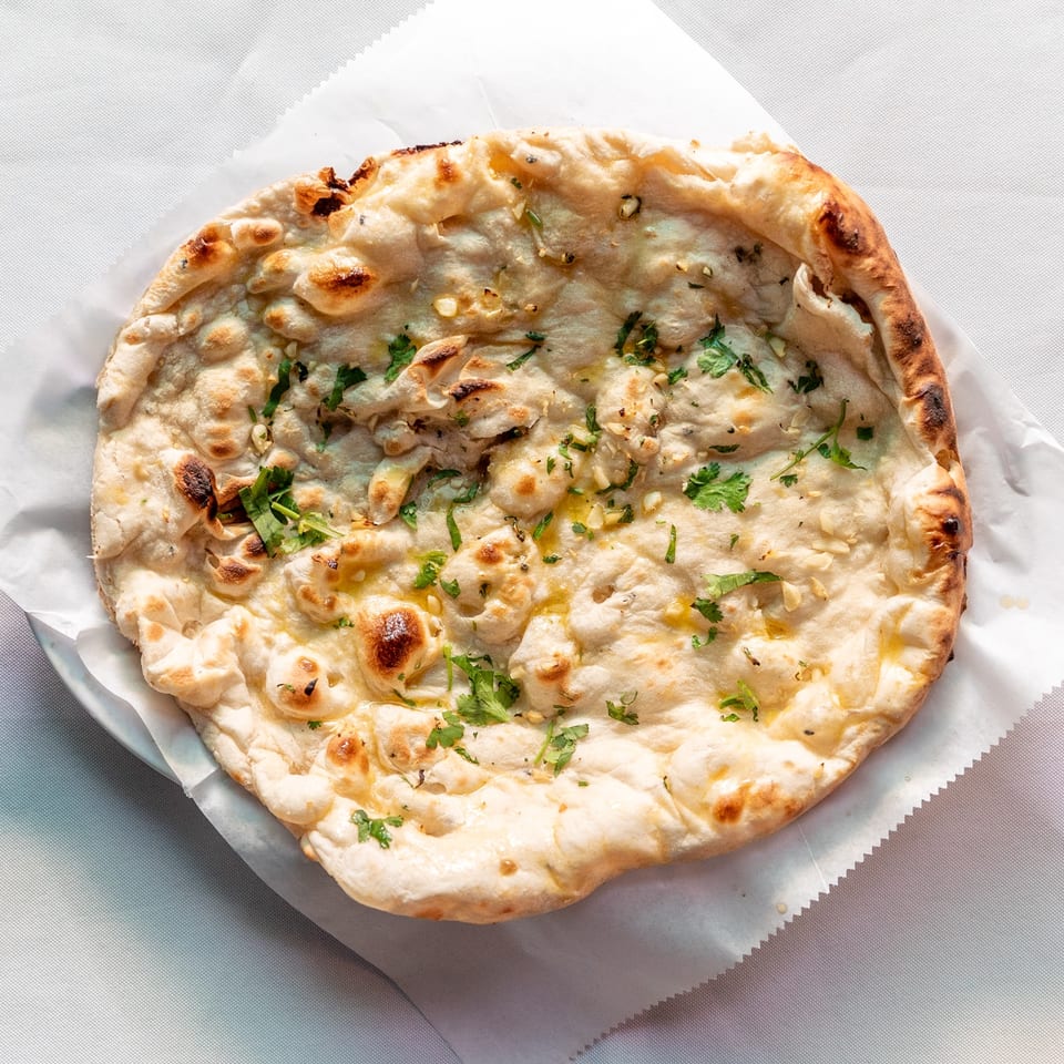 Golden-brown naan bread, topped with garlic, cilantro, and melted butter, on white paper.