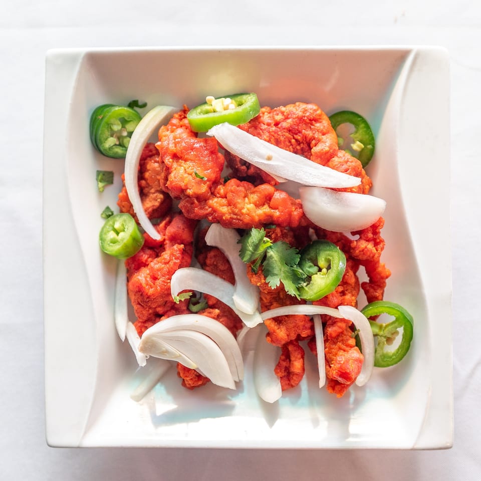 Bright orange fried chicken pieces garnished with white onion slices, green jalapeños, and cilantro.